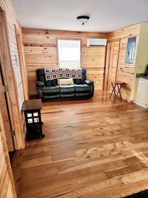 Una habitación con paredes de paneles de madera, un sofá de cuero negro con cojines estampados, una mesita y una lámpara en el techo.