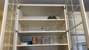 Un armario de cocina con estantes que contienen diverso menaje, incluyendo platos, tazones y cristalería.