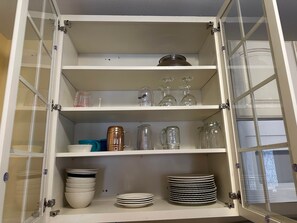 A kitchen cabinet with shelves containing various kitchenware, including plates, bowls, and glassware.