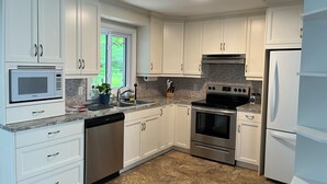 A modern kitchen with white cabinets, stainless steel appliances, and a window providing natural light. - Cozy Countryside Retreat (Clarence-Rockland)