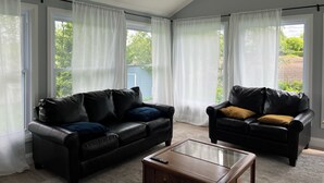 A living room with two black leather sofas, a glass coffee table, and white curtains. - Cozy Countryside Retreat (Clarence-Rockland)