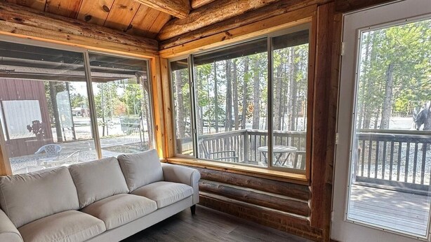 Et interiør i en hytte med sofa, store vinduer og en træterrasse.