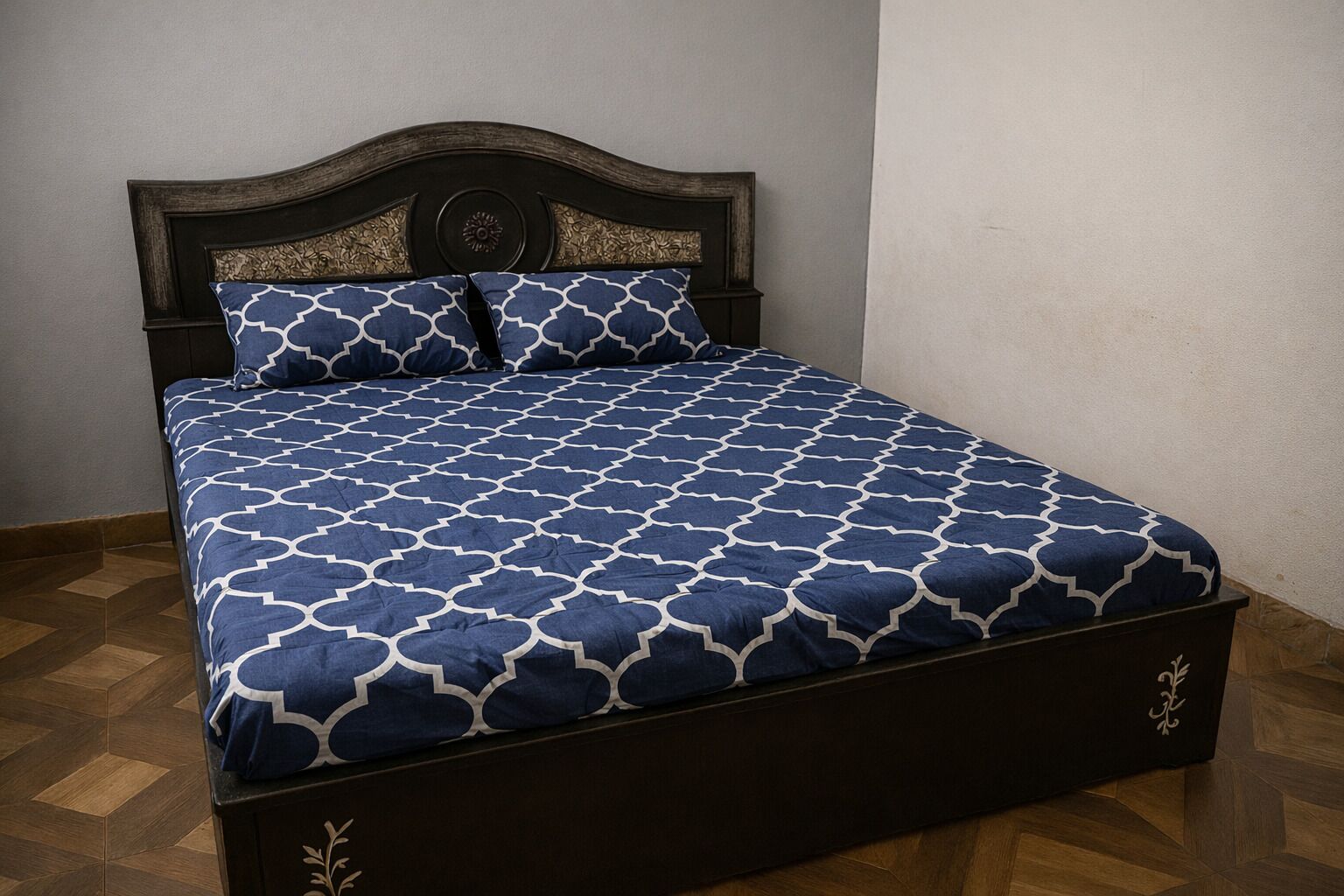 A bed with a dark wooden headboard and a blue patterned bedspread.