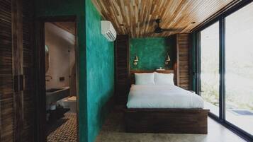 A modern bedroom with a wooden ceiling, a green accent wall, a large bed, and a view through a glass door.