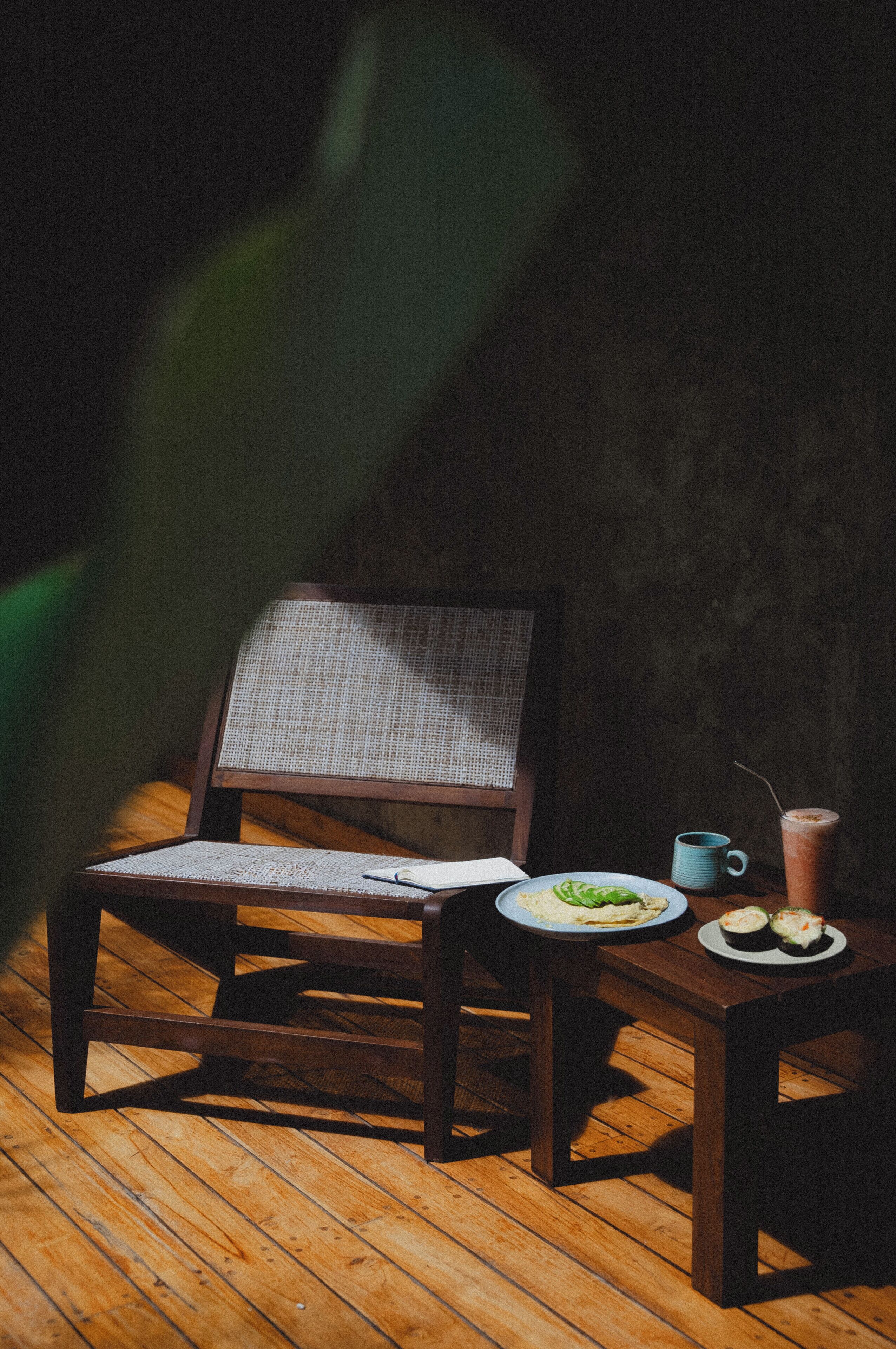 A wooden chair with a woven backrest and a table with a plate of food and a mug.