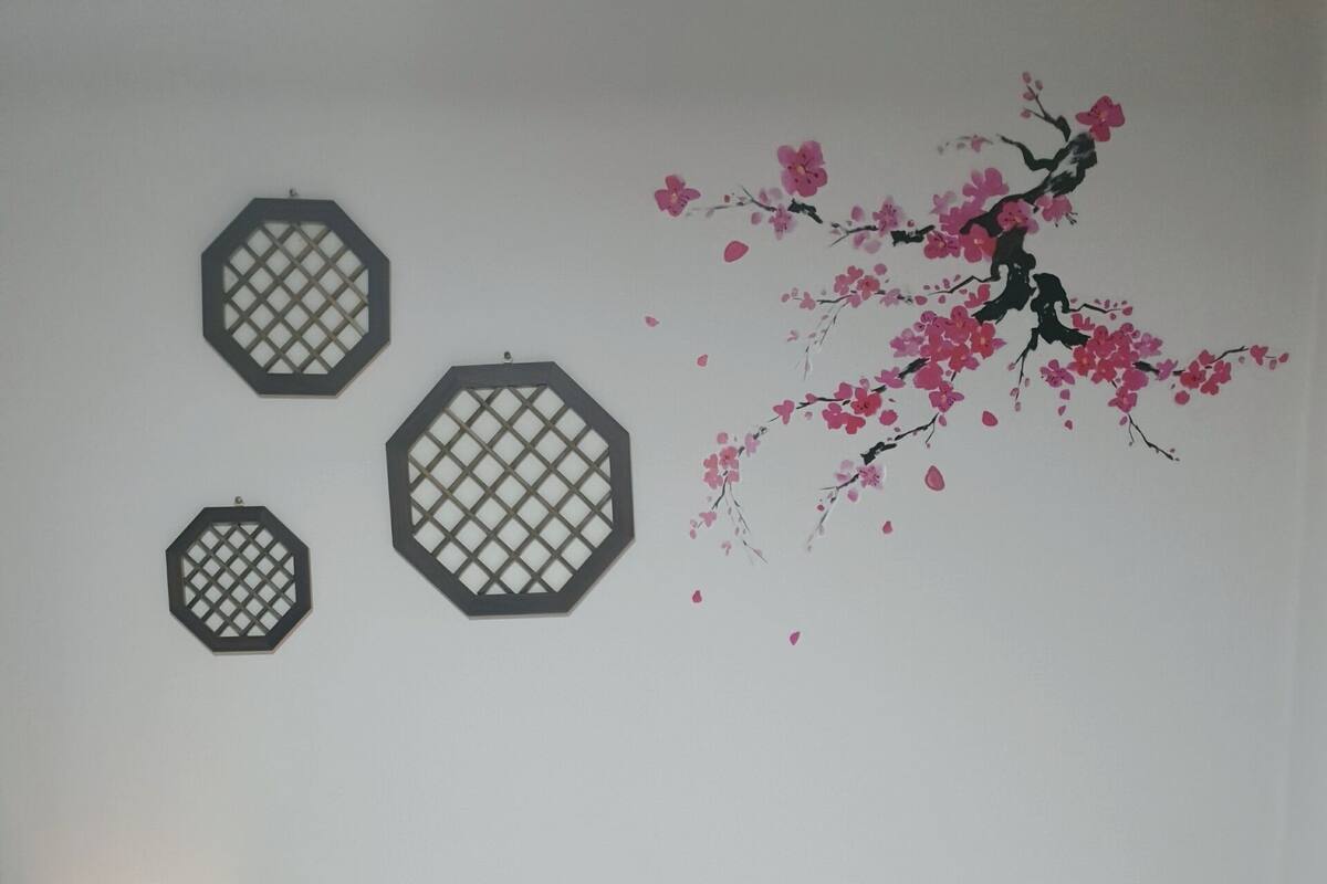 A bedroom with a bed, a nightstand with a lamp, and wall decorations including octagonal frames and a cherry blossom mural.