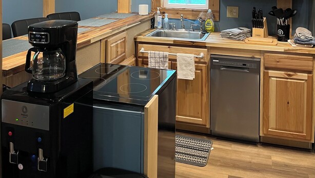 A modern kitchen with wooden cabinets, a built-in dishwasher, a coffee maker, and a window with blinds. - Clinch Mountain Reserve Cabin #2.  Cabin retreat near charming Rogersville, TN. (Rogersville)
