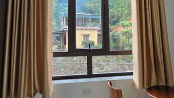 Ein Zimmer mit einem großen Fenster, einem Holzstuhl, einem kleinen Tisch und einem Paar Hausschuhen auf dem Boden.