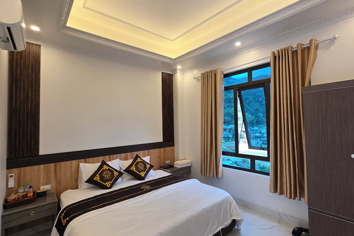A hotel room with a bed, a nightstand, a wardrobe, and a window with curtains.