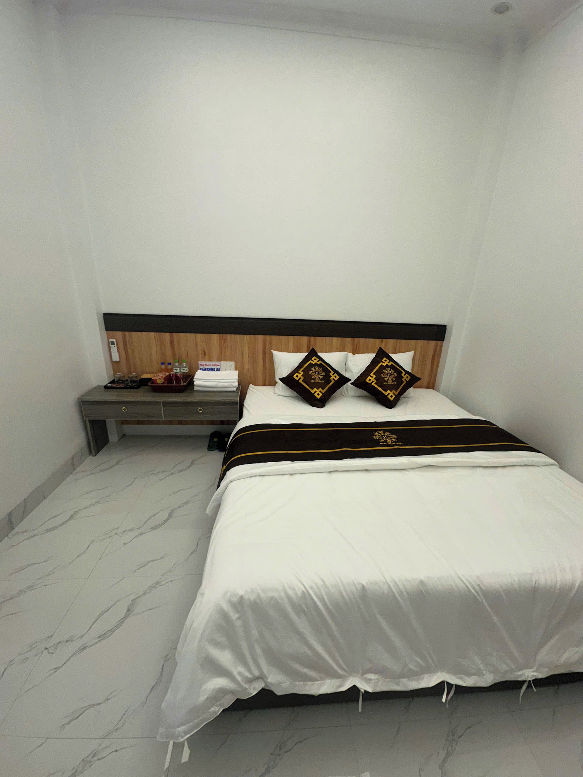 Habitación de hotel con cama, mesita de noche y una pequeña mesa con una botella de agua y una caja de pañuelos.