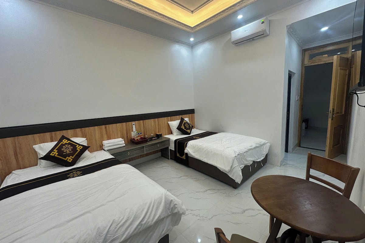 A hotel room with two beds, a small table, and a chair.
