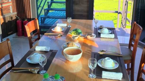 A dining table set with plates, bowls, and glasses, with a view of a green landscape through large windows. - New Highland Hotel (Mu Cang Chai)