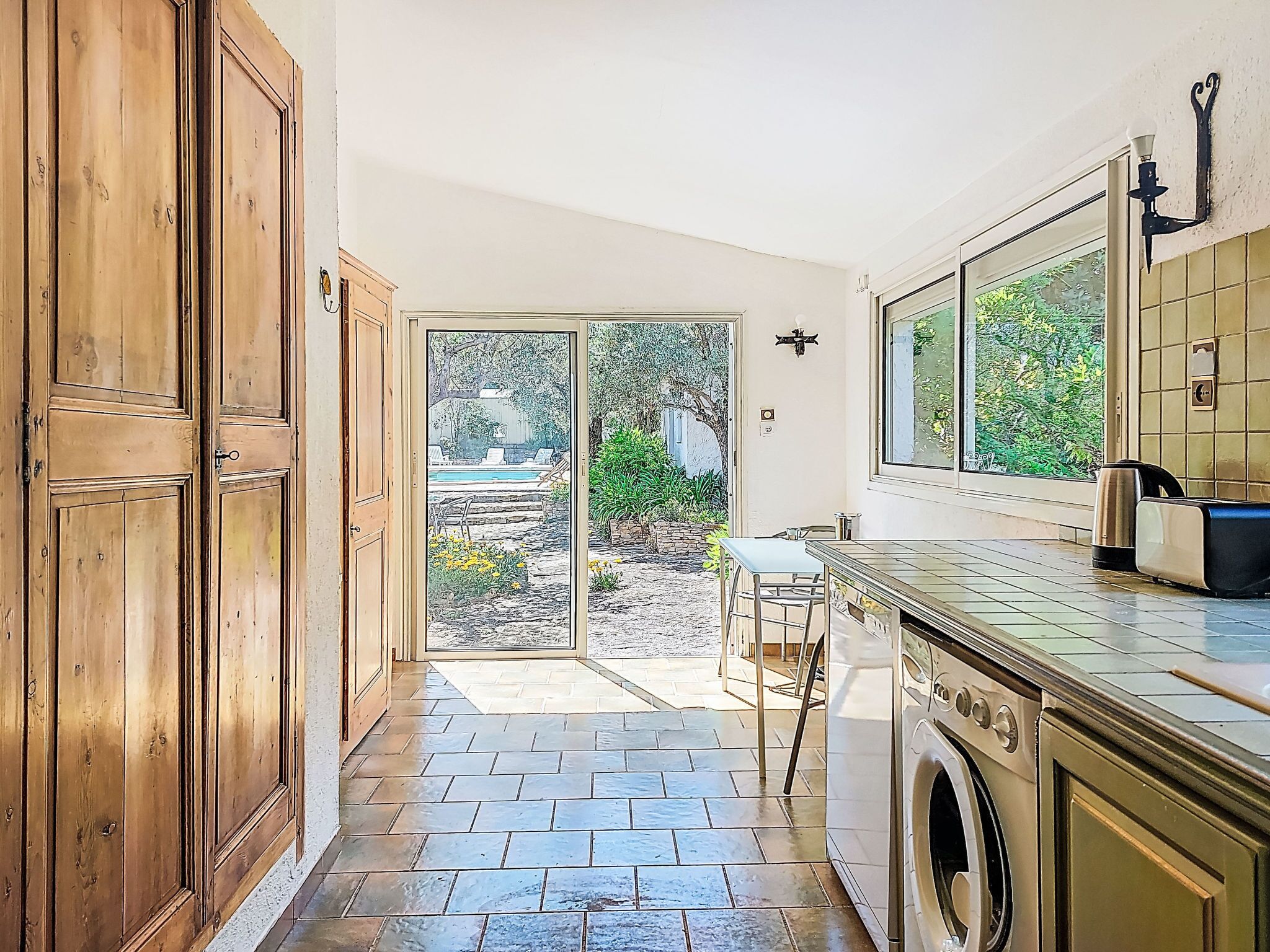 Una cocina con lavadora, un comedor con mesa y sillas, y vistas a un jardín con piscina.