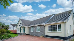 A two-story house with a stone facade, a tiled roof, and a paved driveway. - Audreys - 3 Bed Holiday Home - Manorbier (Tenby)