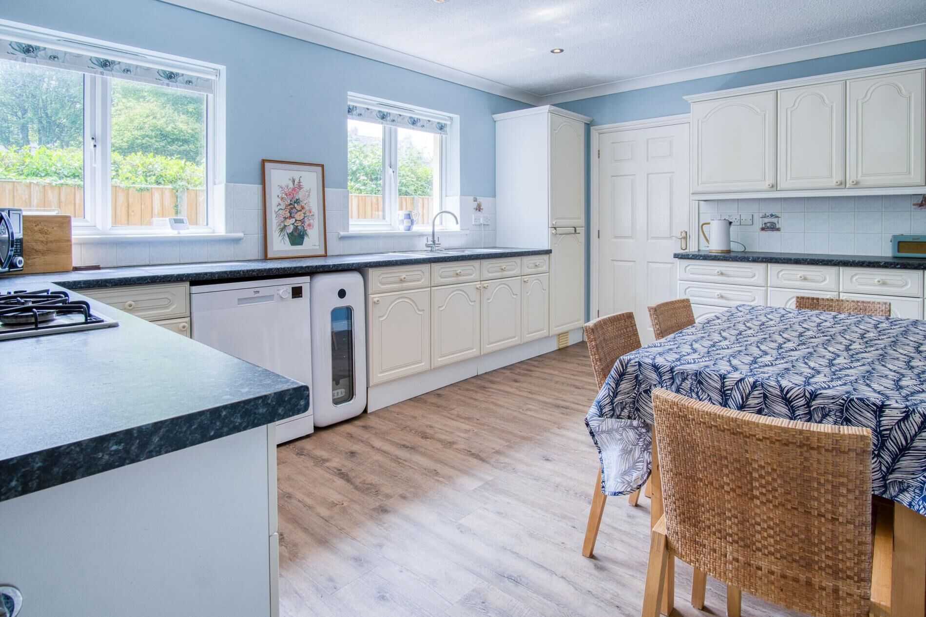 A kitchen with white cabinets, a dining table with chairs, and a view of the outdoors.