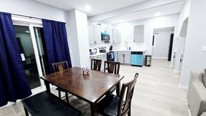 A modern kitchen with white cabinets, a blue dishwasher, and a dining area with a wooden table and chairs. - 3-Bedroom House Close to Pacific University (Forest Grove)