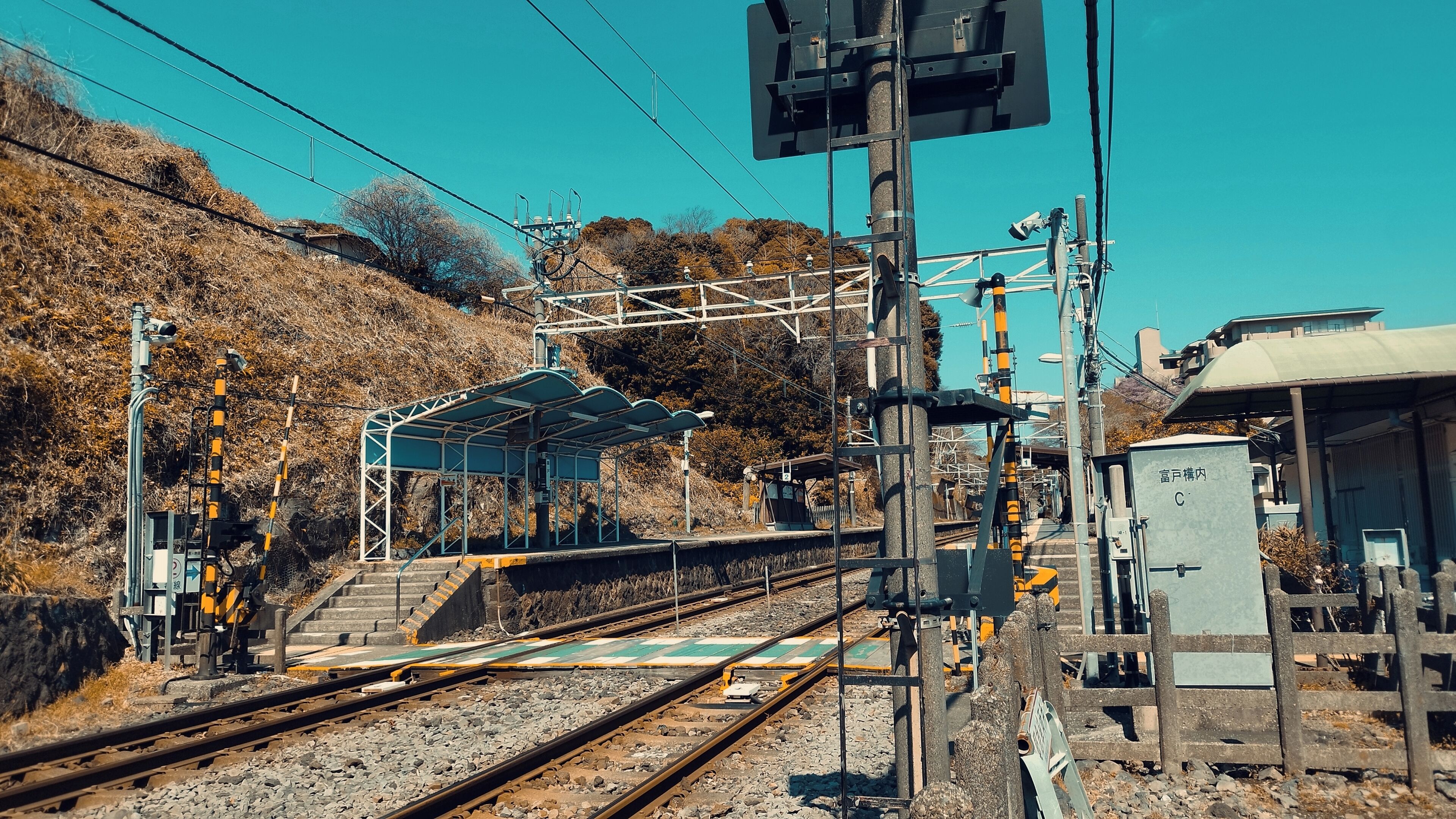 Una estació de tren amb diverses vies, línies elèctriques aeri i una zona d'espera coberta.
