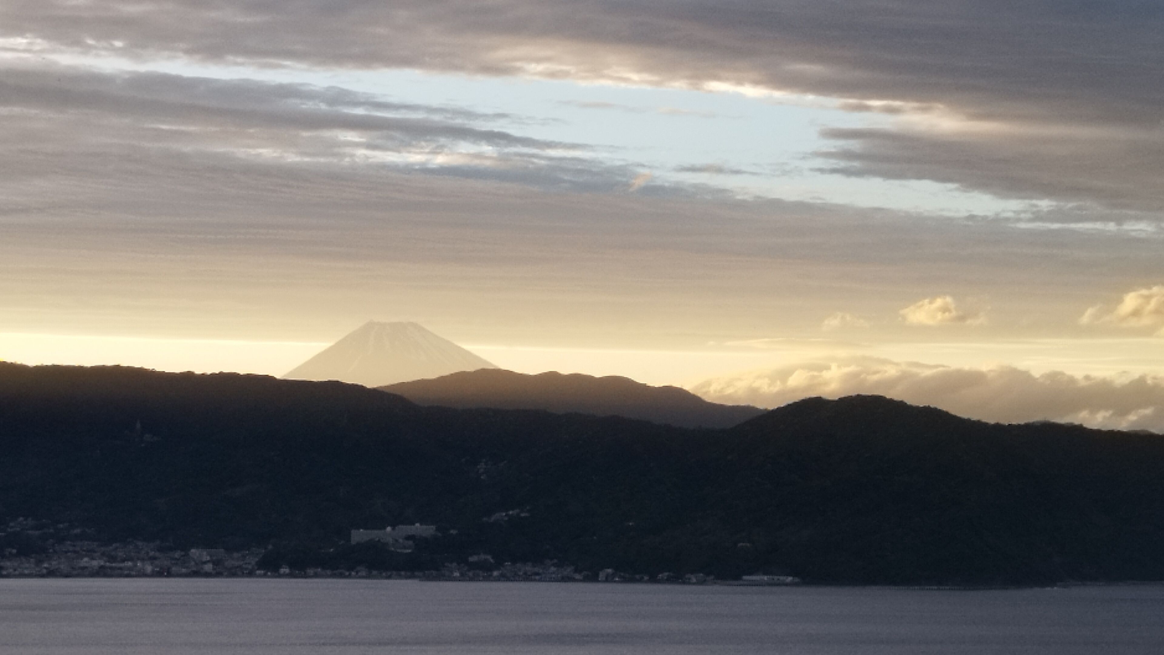 A mountain landscape with a prominent peak, possibly a volcano, and a body of water in the foreground.