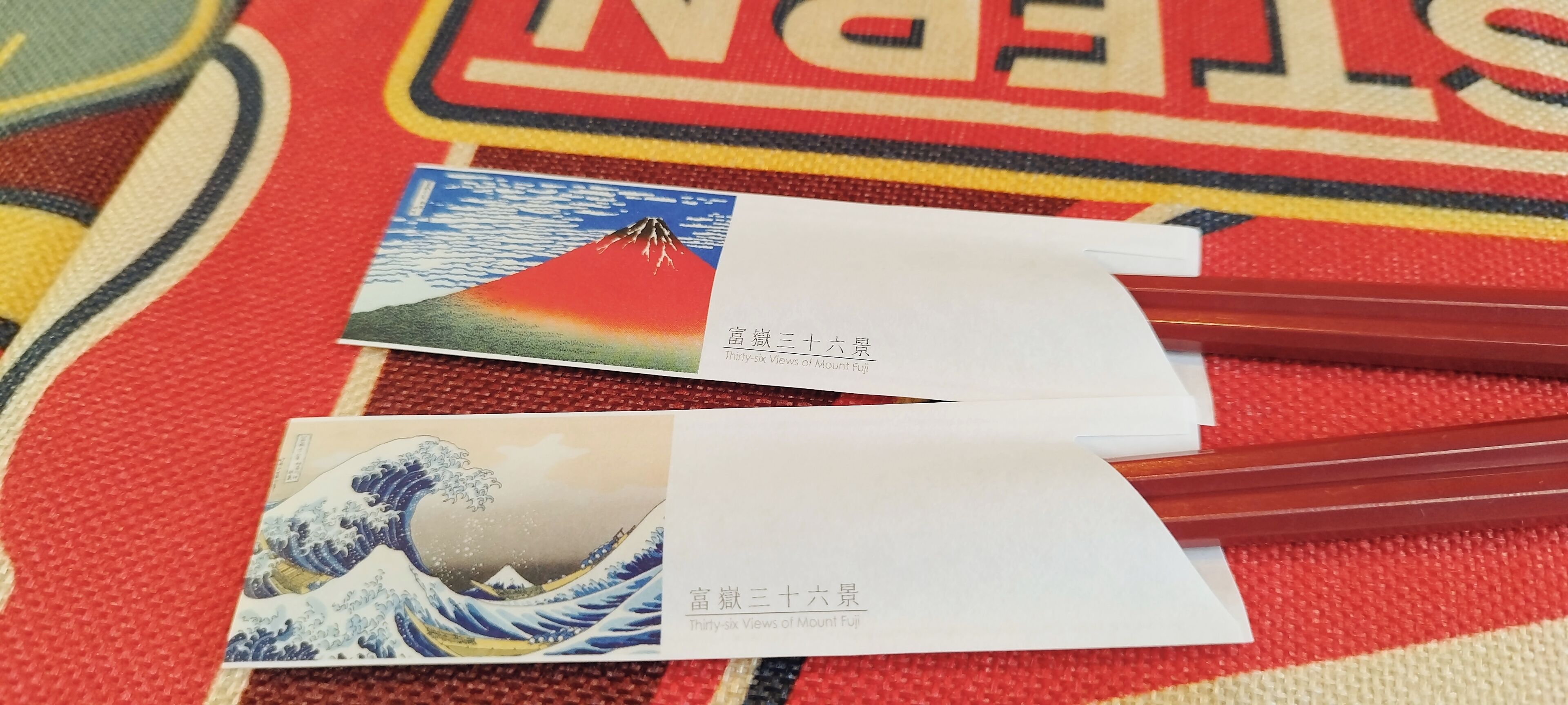 Dues postals amb text japonès i traducció a l'anglès, sobre un teixit de colors amb un dibuix.
