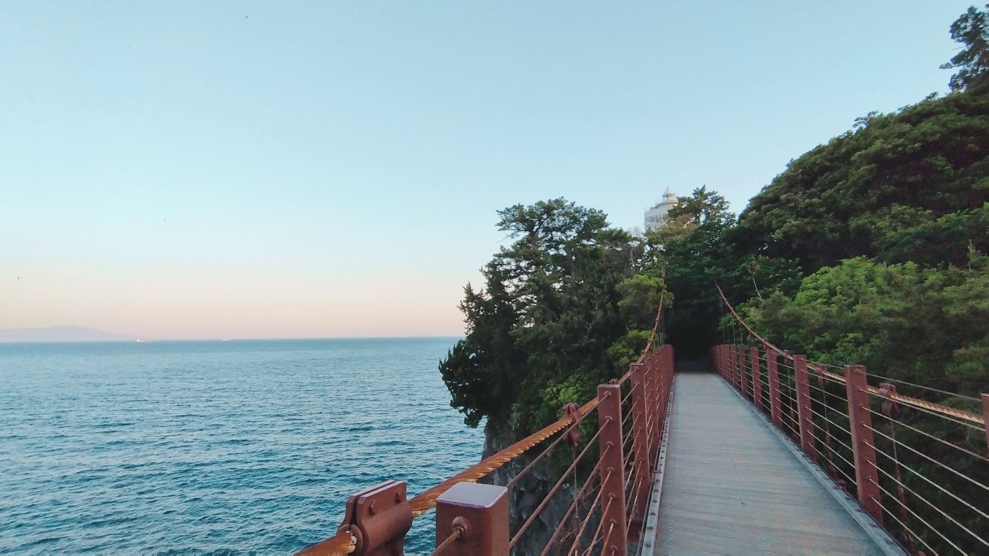 A suspension bridge with a clear view of the sea and distant land.