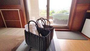 A room with a wooden floor, a black mat, a wicker basket with handles, and a view of greenery through a window. - kokopellihouseizukogen (Ito)