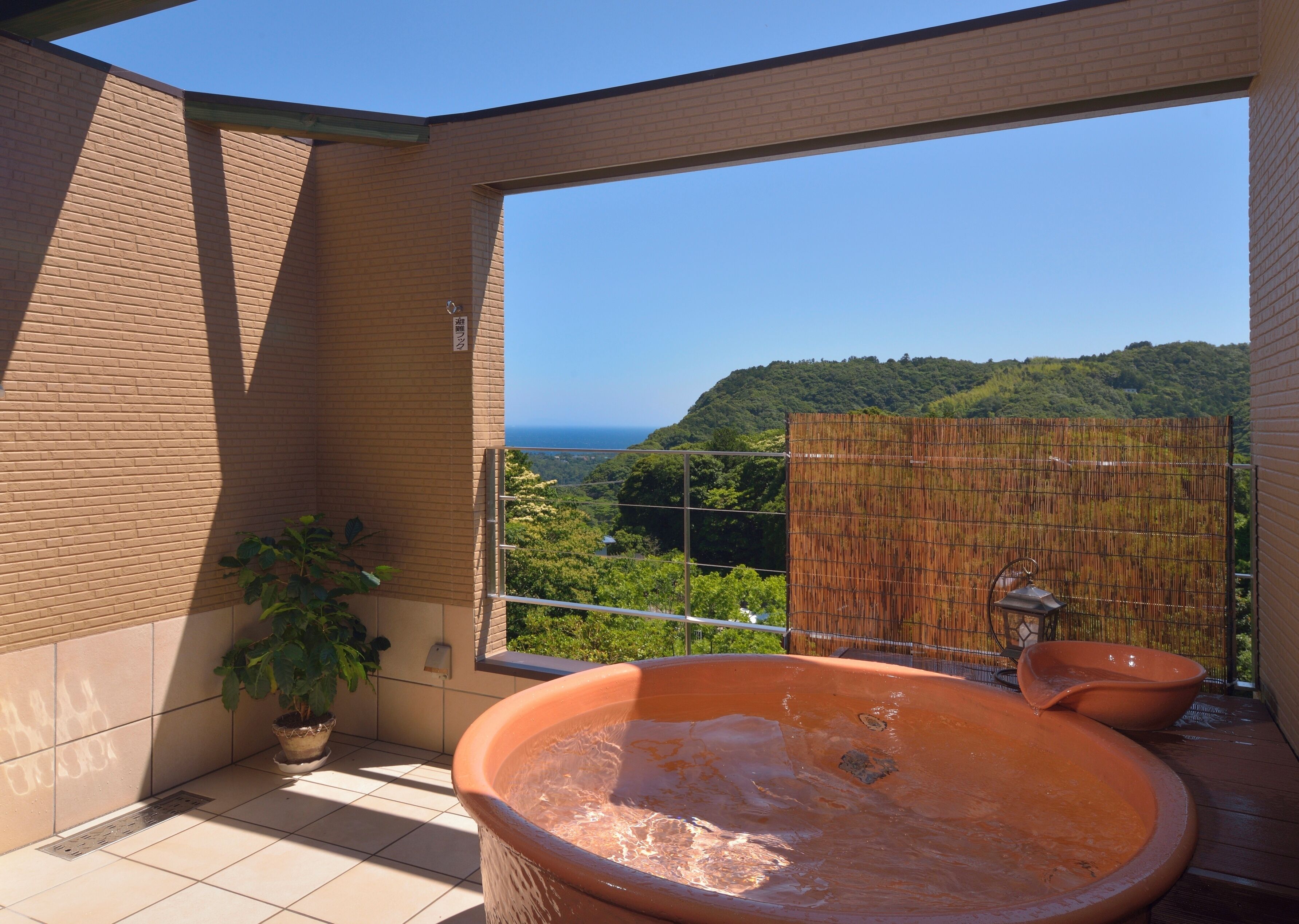 Un bagno con una vasca da bagno grande, una pianta in vaso e vista su una collina boscosa.