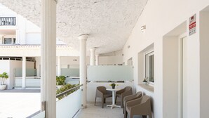 Pasillo de hotel con techo blanco, columnas, una pequeña mesa con sillas y un ventanal.