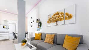 Una sala moderna con un sofá gris, cojines amarillos, una mesa de centro blanca y un reloj de pared.