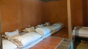 A room with a long wooden bed with white bedding, a wooden floor, and orange walls. - Homestay Khám Phá Y Tý (Y Ty)