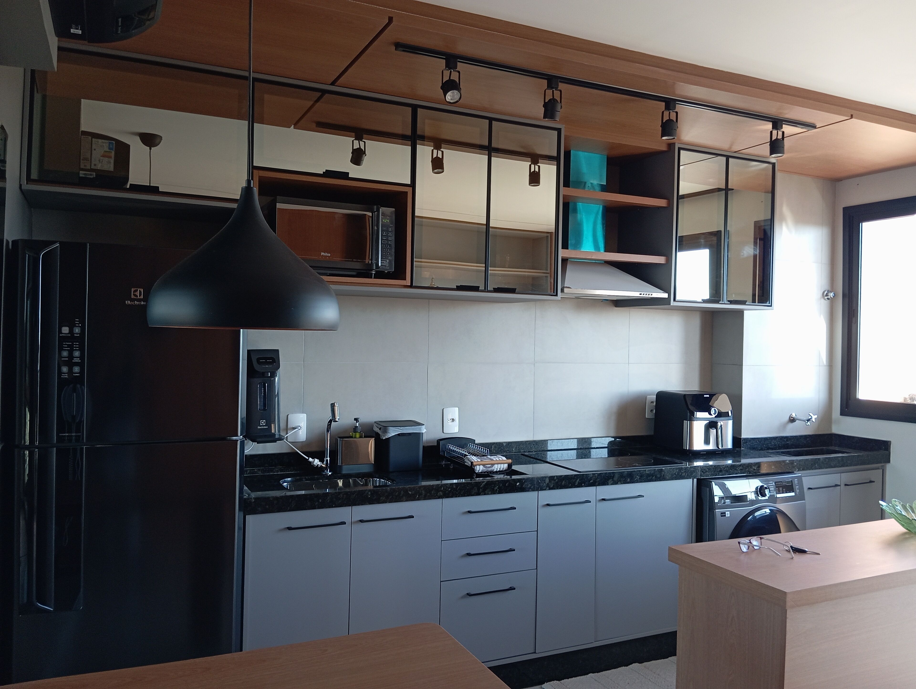A modern kitchen with a refrigerator, stove, and microwave. There are cabinets, a sink, and a window providing natural light.