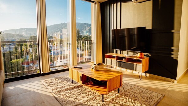 A modern living room with a large TV, wooden furniture, and a view of a cityscape through large windows.