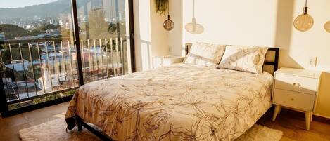 A bedroom with a large bed, a nightstand, a bedside table, and a view of a cityscape through a large window.