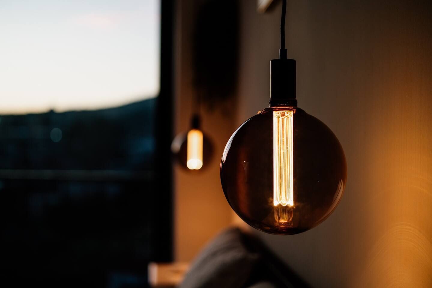 A hanging light bulb with a visible filament, a wall socket, and a window with a view of the outside.