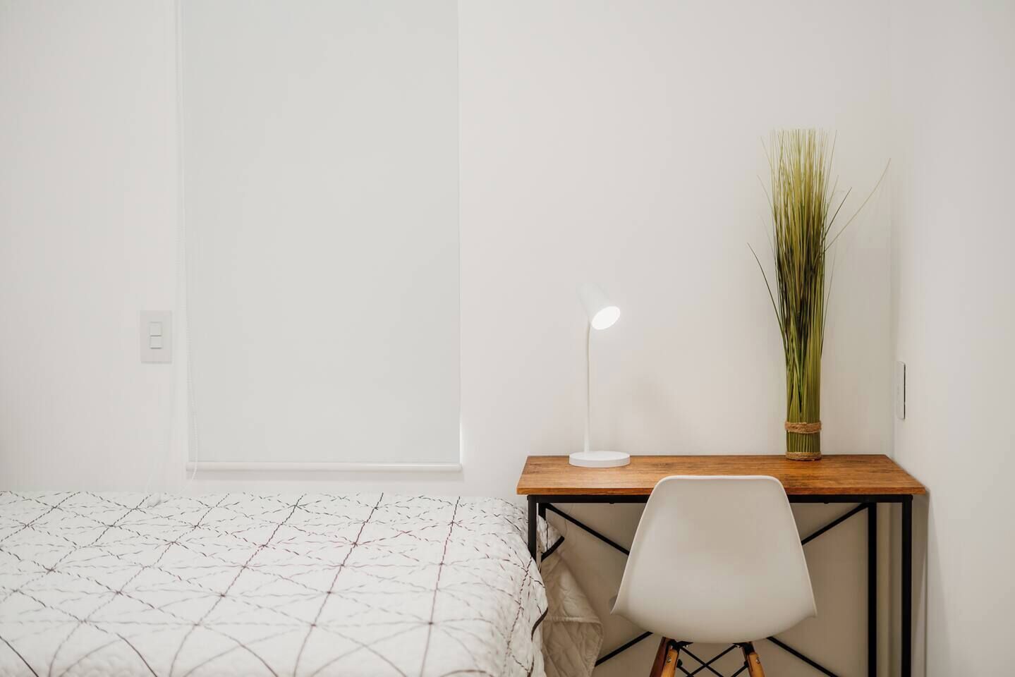 A bedroom with a bed, a desk with a lamp, and a chair.