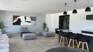 A modern living room with a sectional sofa, ottomans, a dining area with bar stools, and pendant lighting.