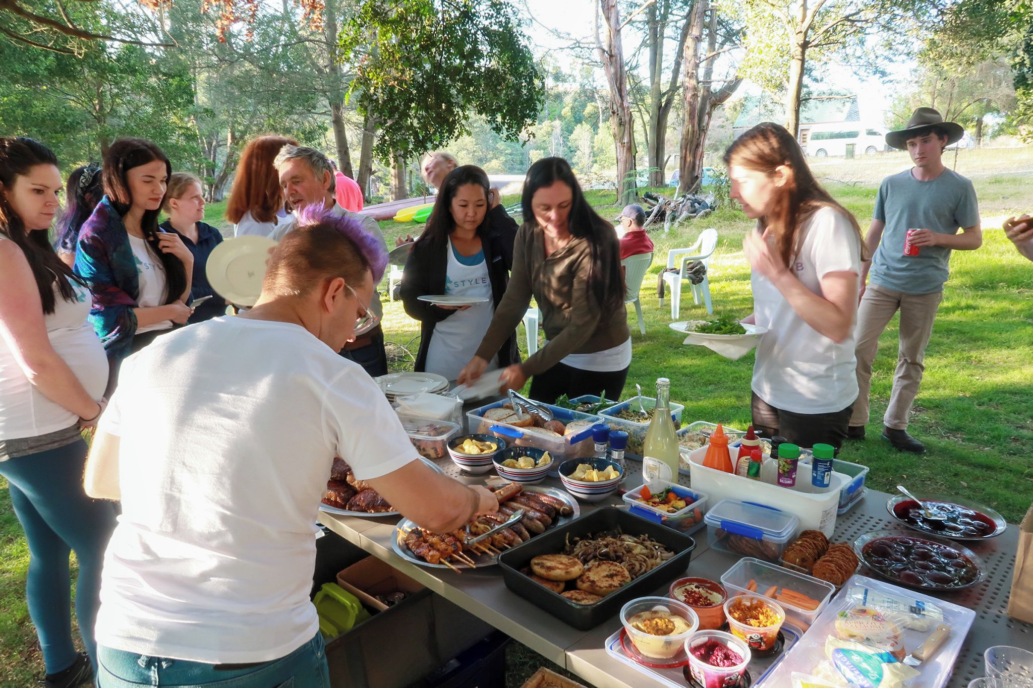 Een groep mensen staat rond een buffet met verschillende gerechten en toevoegingen.