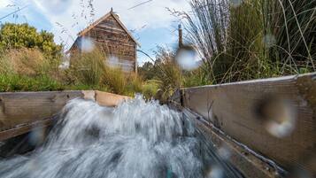 A wooden bridge over a flowing stream with a rustic building in the background.