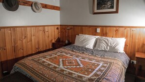 Une chambre aux murs lambrés, avec un lit, des oreillers, une courtepointe et un porte-chapeaux fixé au mur.