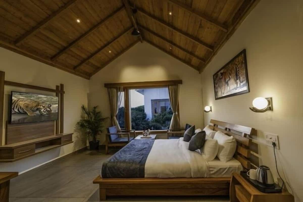 A bedroom with a wooden ceiling, a bed with pillows, a nightstand with a kettle, and a painting of a tiger.