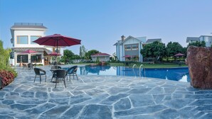 A swimming pool with stone tiles, outdoor furniture, and umbrellas. - Quinta Premium Resort, Corbett (Kaladhungi)