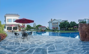A swimming pool with stone tiles, outdoor furniture, and umbrellas.