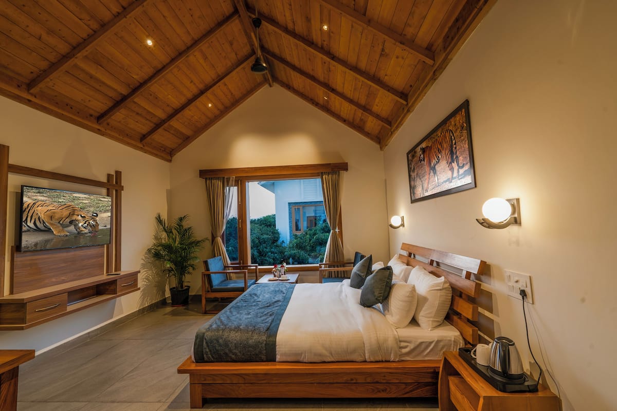 A bedroom with a wooden ceiling, a bed with pillows, a nightstand, a TV, and a window with curtains.