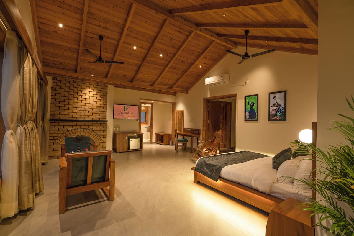 A spacious bedroom with a large bed, wooden ceiling beams, a brick wall, and a fireplace.