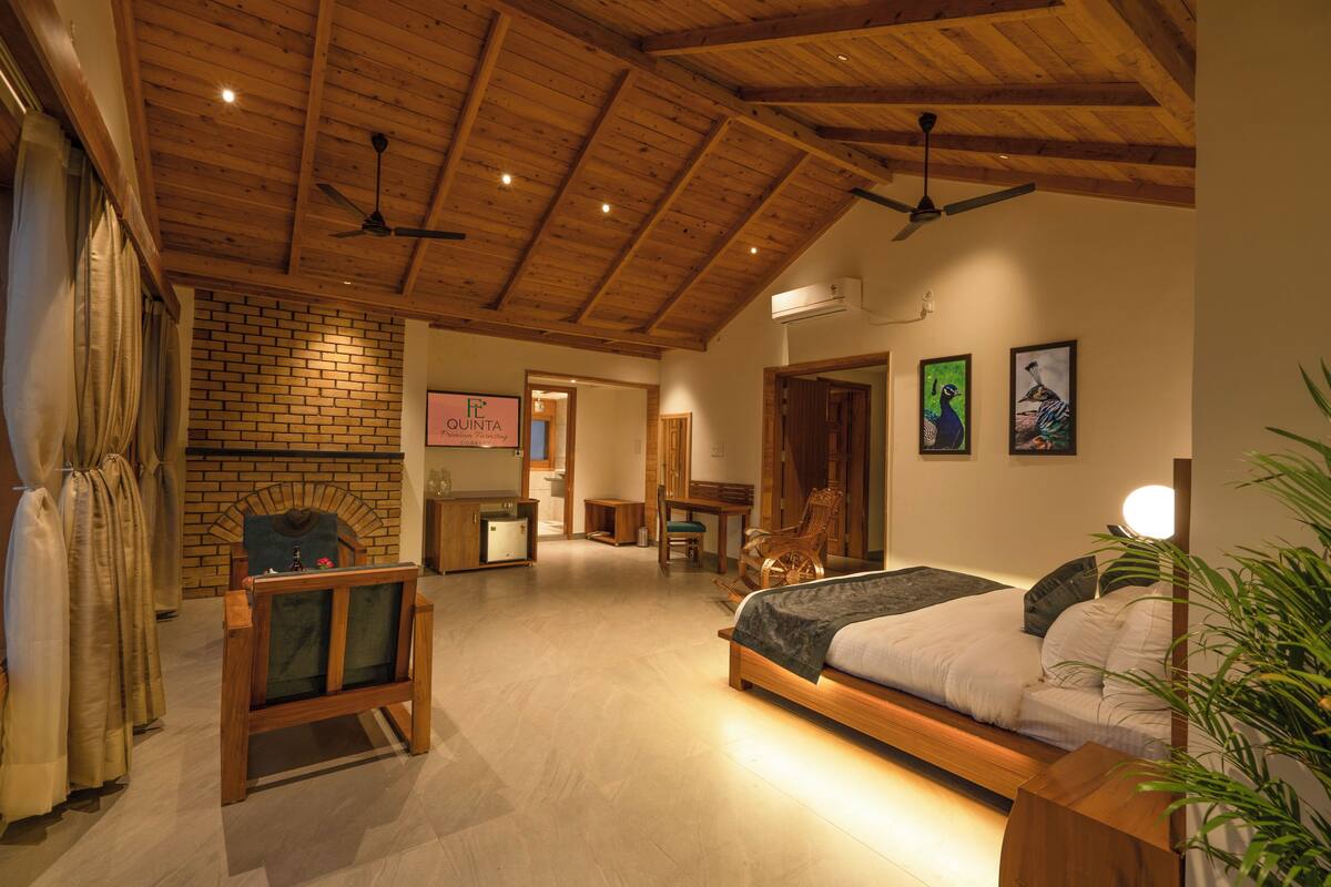 A spacious bedroom with a large bed, wooden ceiling beams, a brick wall, and a fireplace.