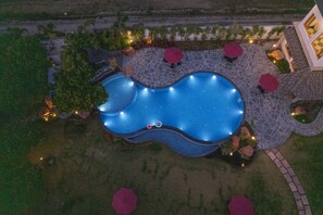 An aerial view of a swimming pool with a stone deck, surrounded by trees and outdoor seating areas. - Quinta Premium Resort, Corbett (Kaladhungi)