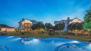 A swimming pool with a tiled edge, surrounded by a well-maintained lawn and trees. - Quinta Premium Resort, Corbett (Kaladhungi)