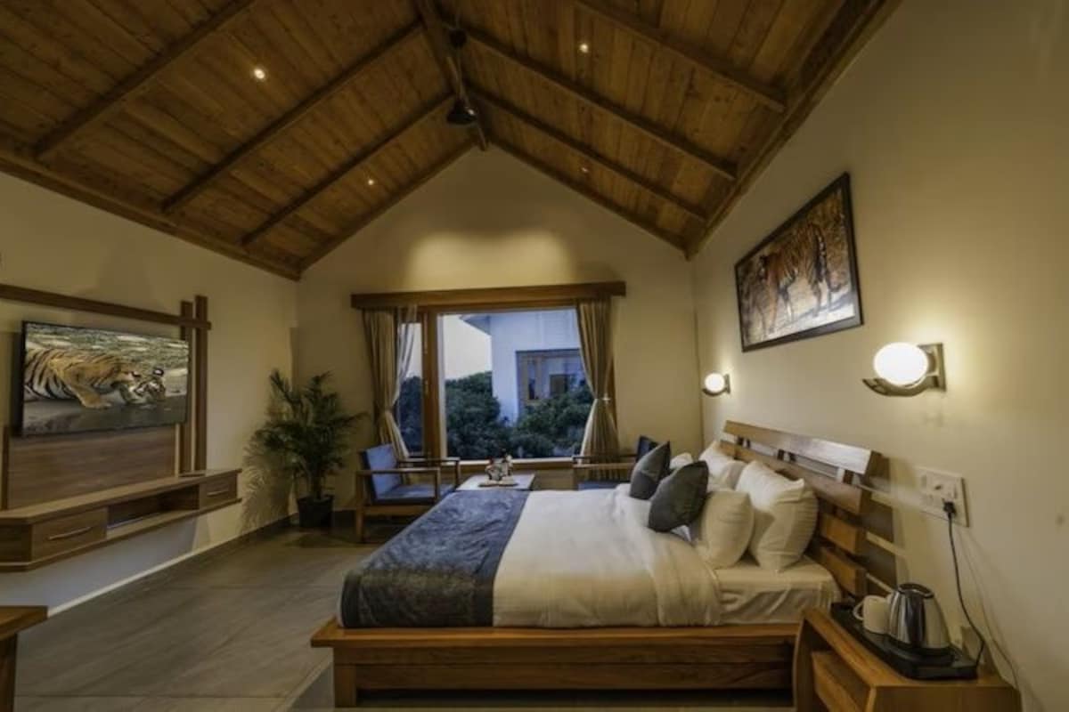 A bedroom with a wooden ceiling, a bed with pillows, a nightstand with a kettle, and a painting of a tiger.