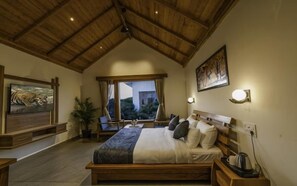 A bedroom with a wooden ceiling, a bed with pillows, a nightstand with a kettle, and a painting of a tiger. - Quinta Premium Resort, Corbett (Kaladhungi)