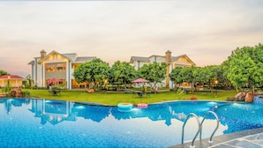 A swimming pool with a tiled edge, surrounded by a well-maintained lawn and trees. - Quinta Premium Resort, Corbett (Kaladhungi)