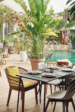 An outdoor dining area with a pool, potted plants, and wicker furniture. - Hôtel Boma (Dakar)